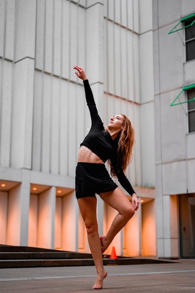 Dancer in coupé relevé barefoot in front of grey city buildings