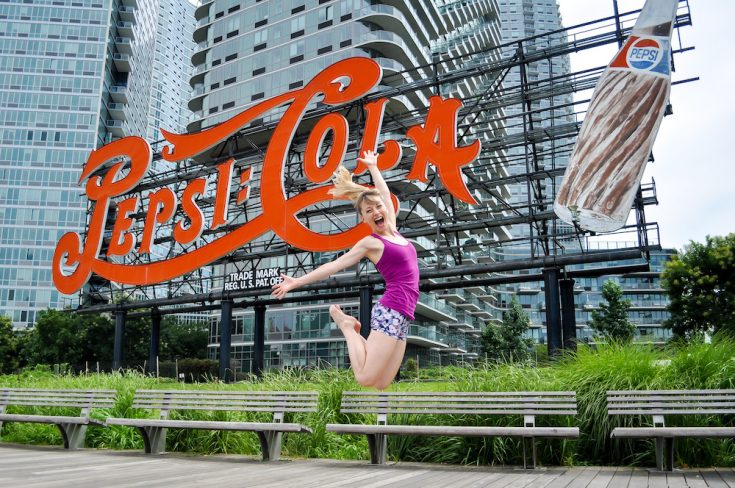 Move With HPA For Dancers founder Heidi Friese jumping for joy in front of Pepsi sign In NYC